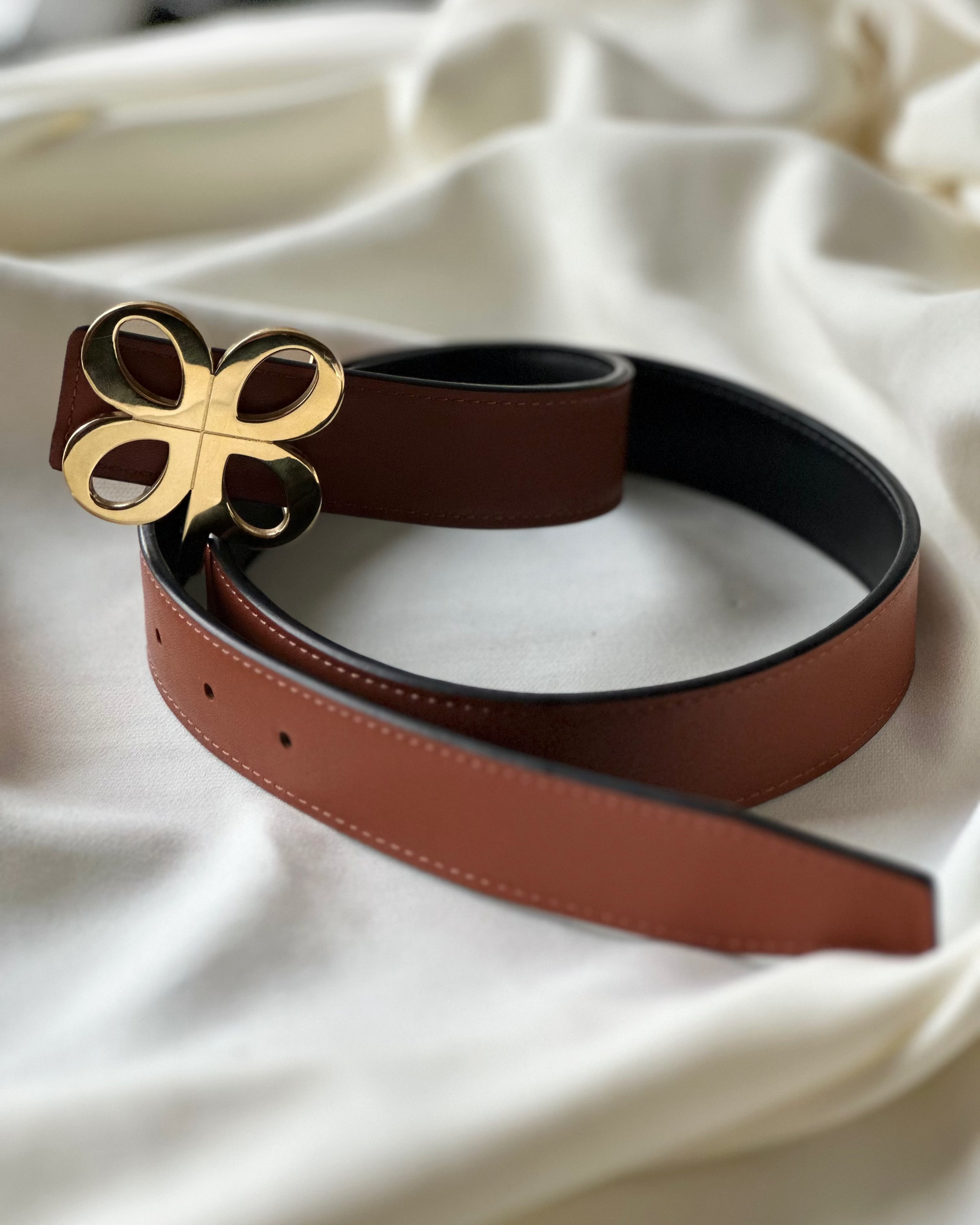Brown leather belt with a gold buckle on a white fabric background