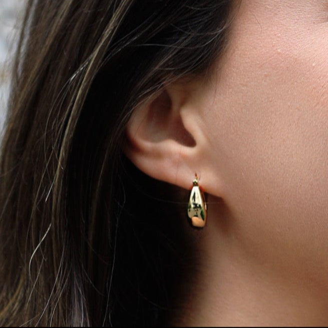 Woman with long dark hair wearing earrings against a textured light gray background