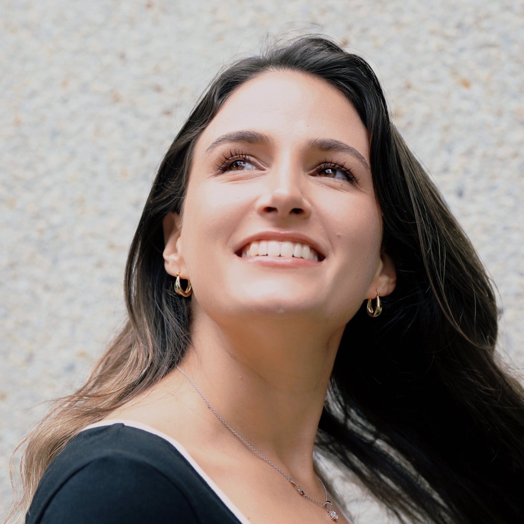 Woman with long dark hair smiling against a textured light gray wall