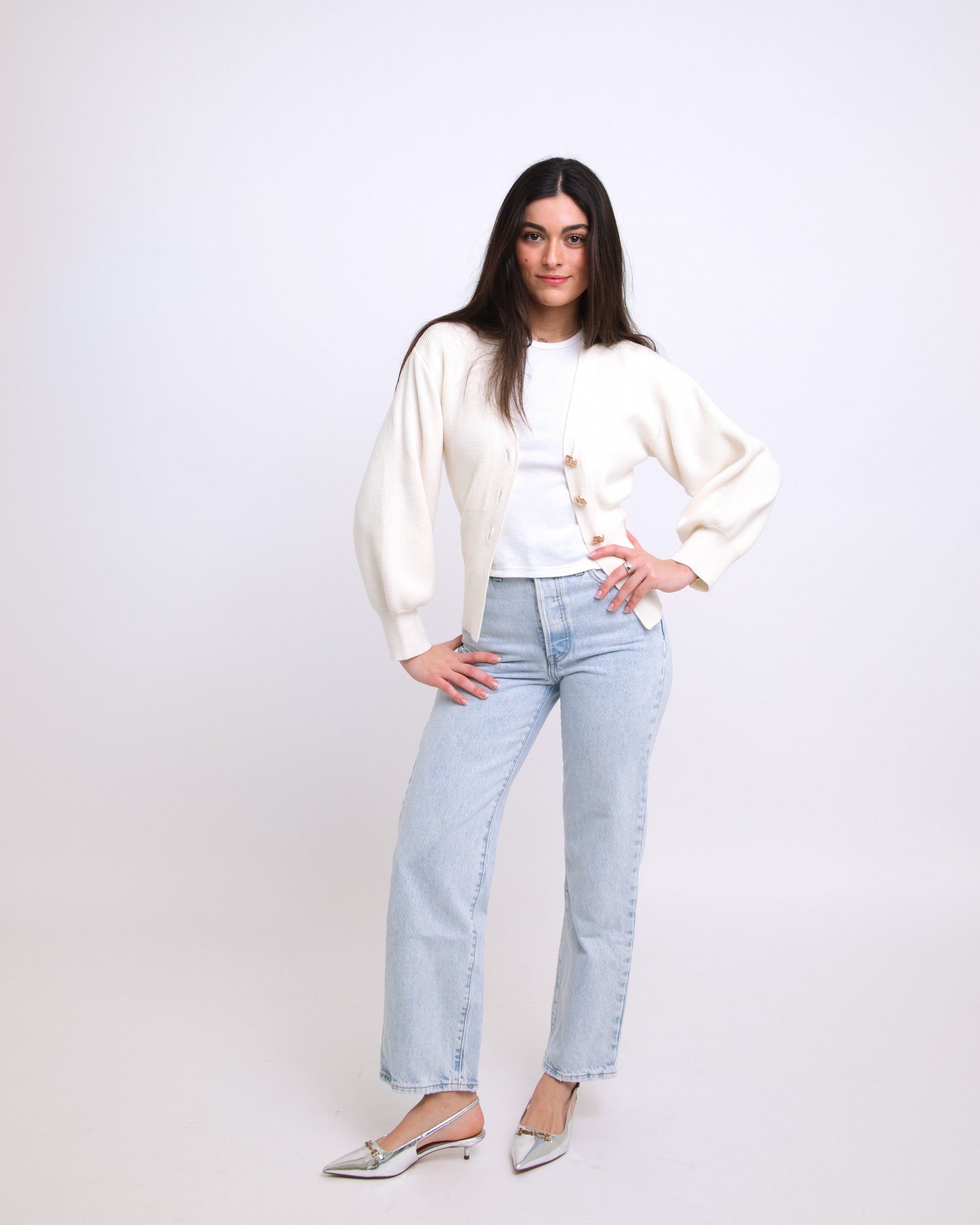 Woman wearing a white blouse and light blue jeans against a plain background