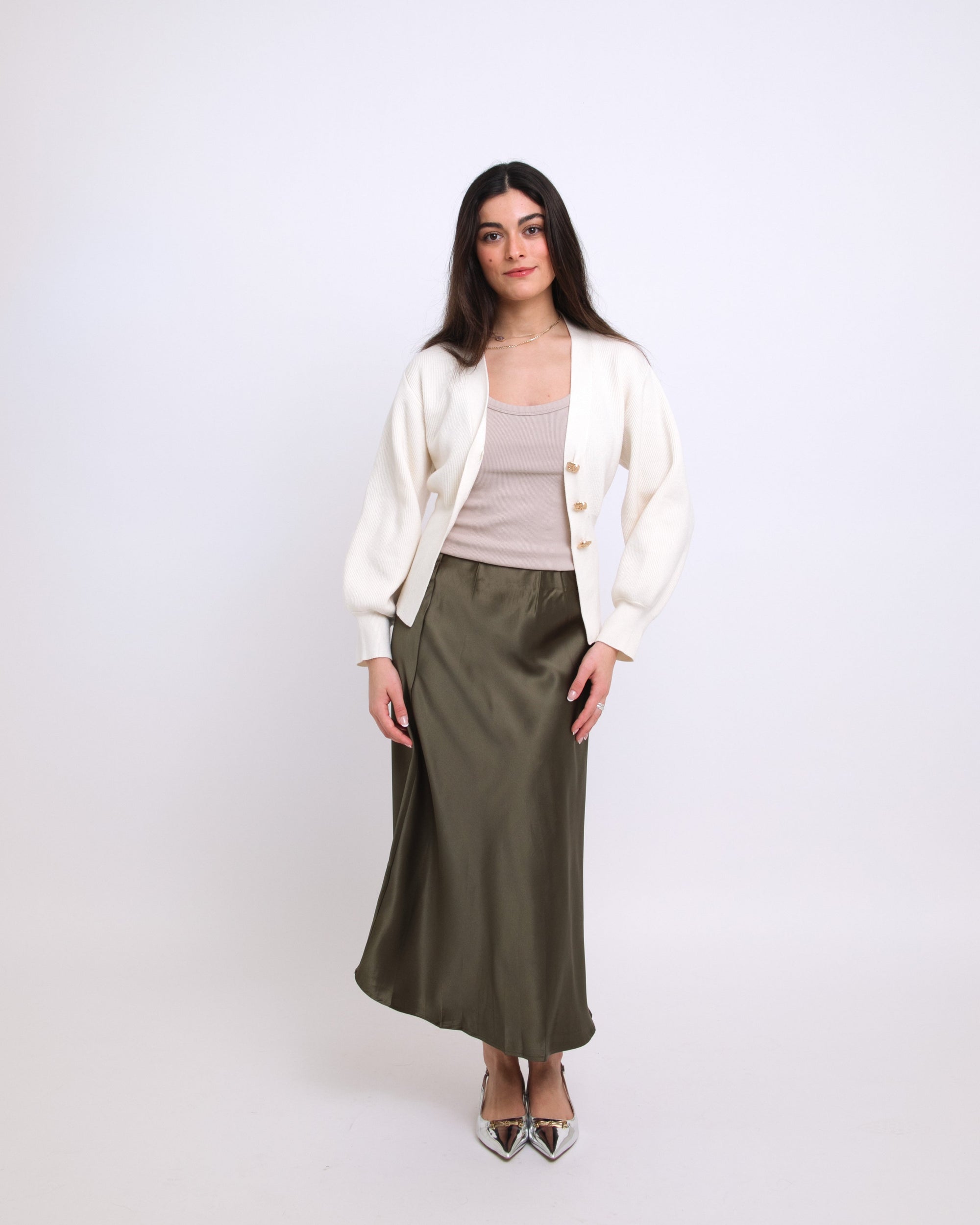Woman wearing a white cardigan, beige top, and green skirt on a white background