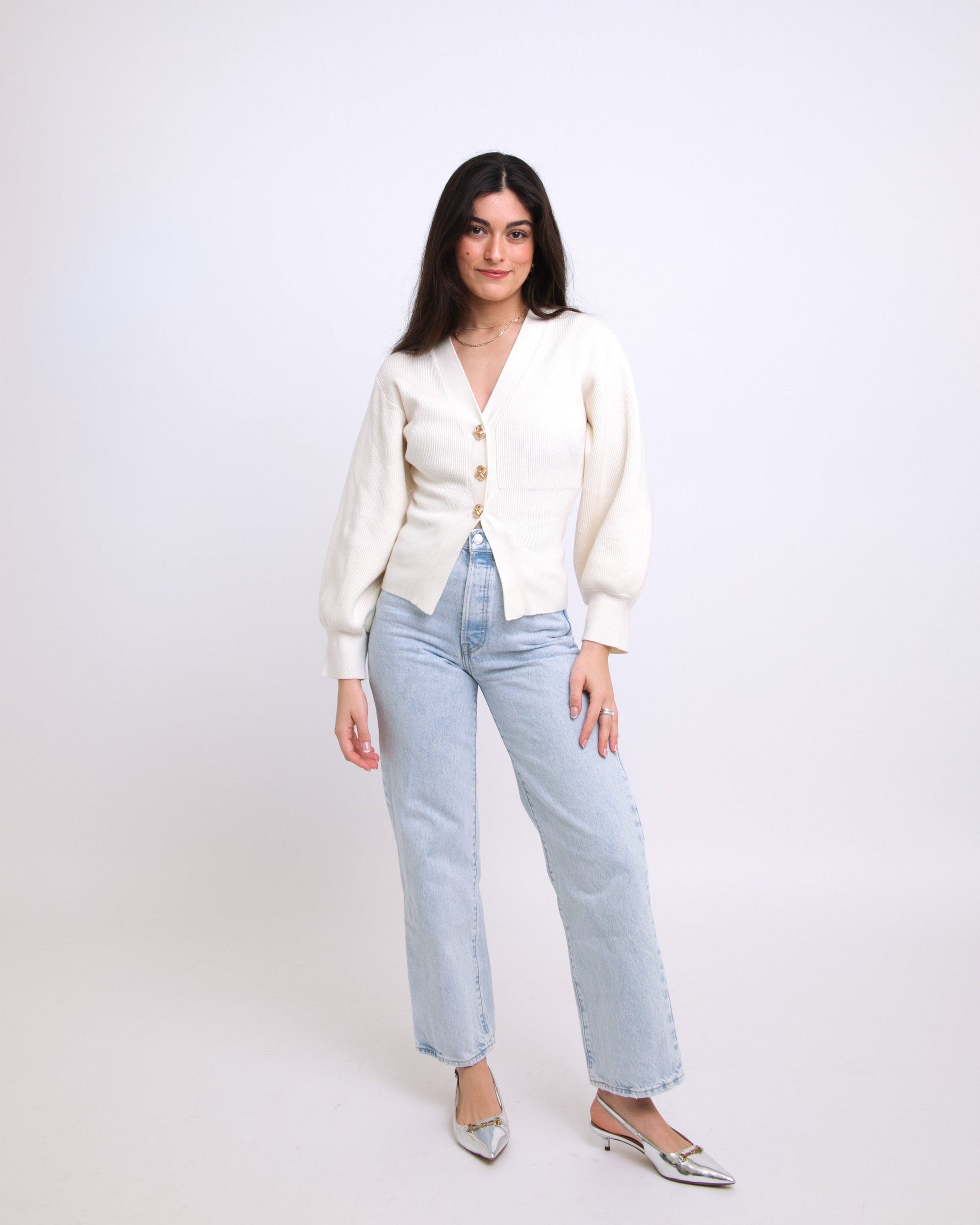 Woman wearing a white cardigan and light blue jeans on a white background