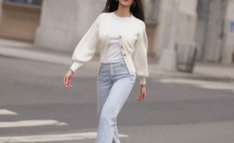 Woman walking on a street wearing a white cardigan, white shirt, and light blue jeans.